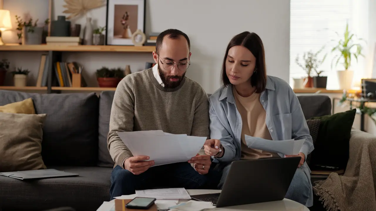couple assis dans le salon vérifiant un contrat de vente de terrain à un promoteur