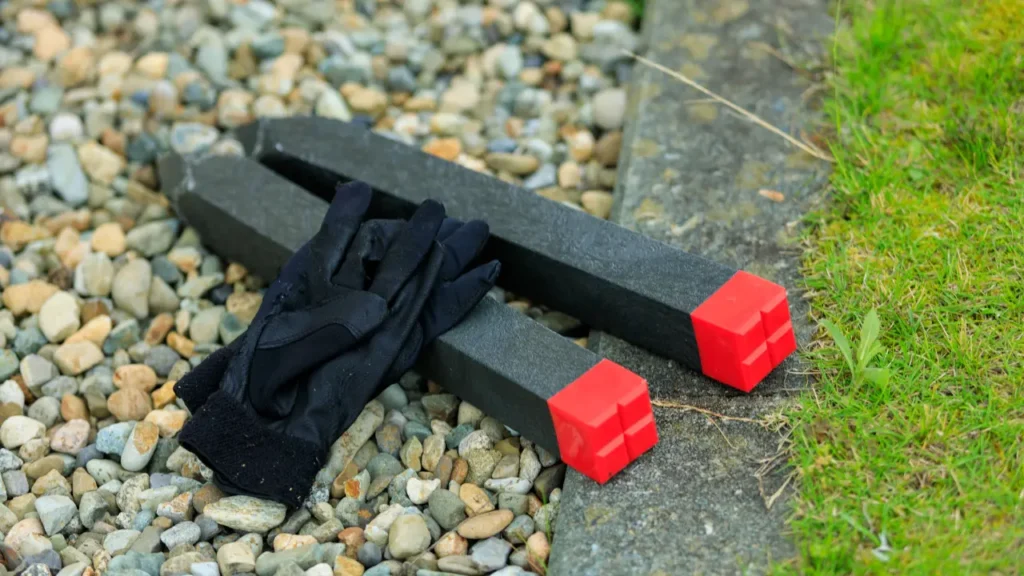 Bornes de bornage en béton avec repères rouges et gants de travail posés sur gravier à la limite d'un terrain gazonné