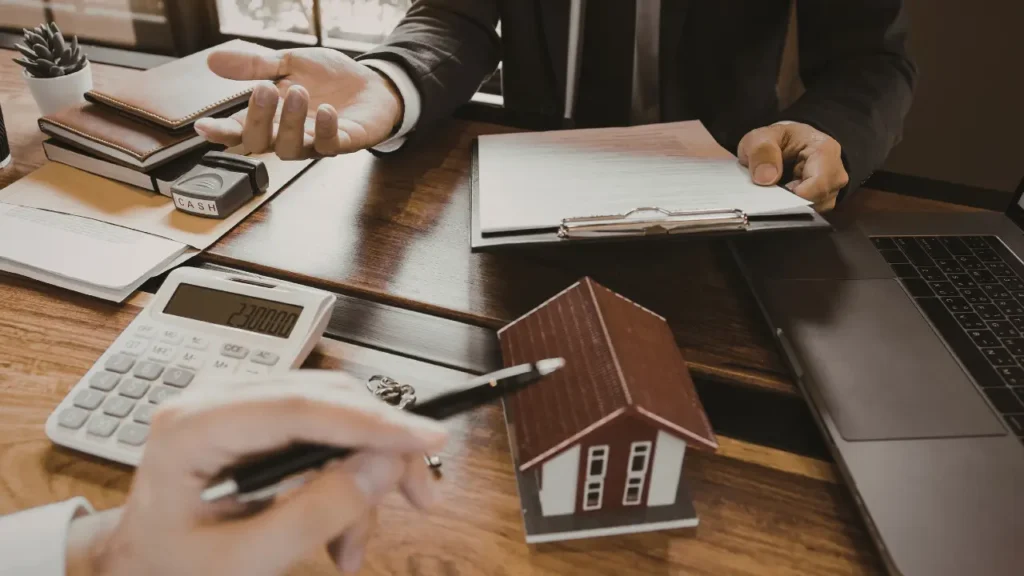 Discussion autour d’un projet immobilier avec maquette de maison, calculatrice et documents financiers, illustration de l’analyse du promoteur Icade en 2026.